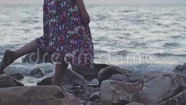 一个穿着长裙子在岩石海滩上慢动作的女人。 3840x2160